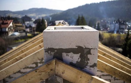 Close-up detail of roof frame of rough wooden lumber beams and chimney made of foam insulation blocks on blurred green background. Building, roofing, construction and renovation concept.